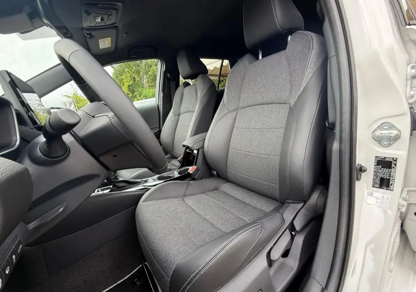 Intérieur côté conducteur de la Toyota Corolla Touring Sport blanche, sièges tissu gris et cuir noir avec surpiqûres blanches.