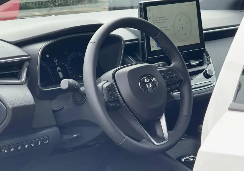 Vue intérieure côté conducteur de la Toyota Corolla Touring Sport blanche, avec volant multifonction et écran tactile central.