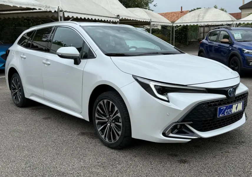 Toyota Corolla Touring Sport blanche nacrée vue en 3/4 avant droit, avec calandre noire et jantes alliage distinctives.