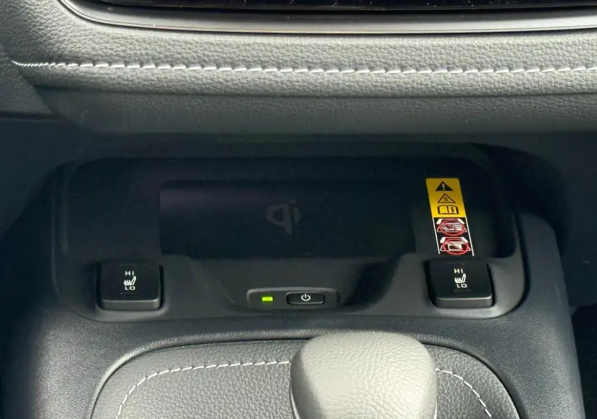 Gros plan sur la console centrale de la Toyota Corolla Touring Sport blanche, montrant les commandes de sièges chauffants et un chargeur sans fil.