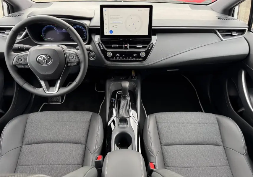 Vue intérieure frontale de la Toyota Corolla Touring Sport 2025, tableau de bord moderne avec écran tactile et sièges gris tissu et cuir.