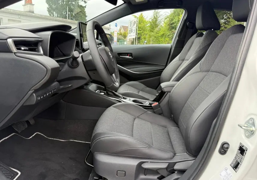 Intérieur de la Toyota Corolla Touring Sport 2025 vue côté conducteur, sièges gris tissu et cuir, tableau de bord moderne.