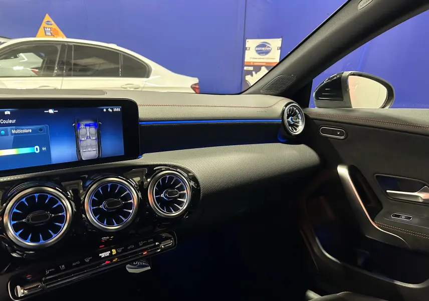 Vue intérieure côté passager de la Mercedes Classe CLA Shooting Brake II 200D AMG noire, avec éclairage d'ambiance bleu et aérateurs ronds.