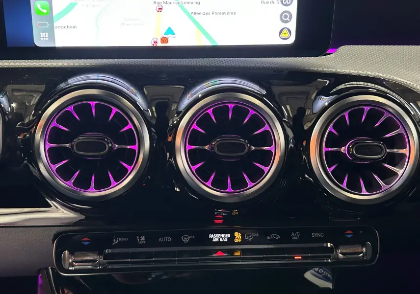 Détail des trois aérateurs ronds illuminés en violet sur le tableau de bord noir brillant d'une Mercedes Classe CLA Shooting Brake 2024.