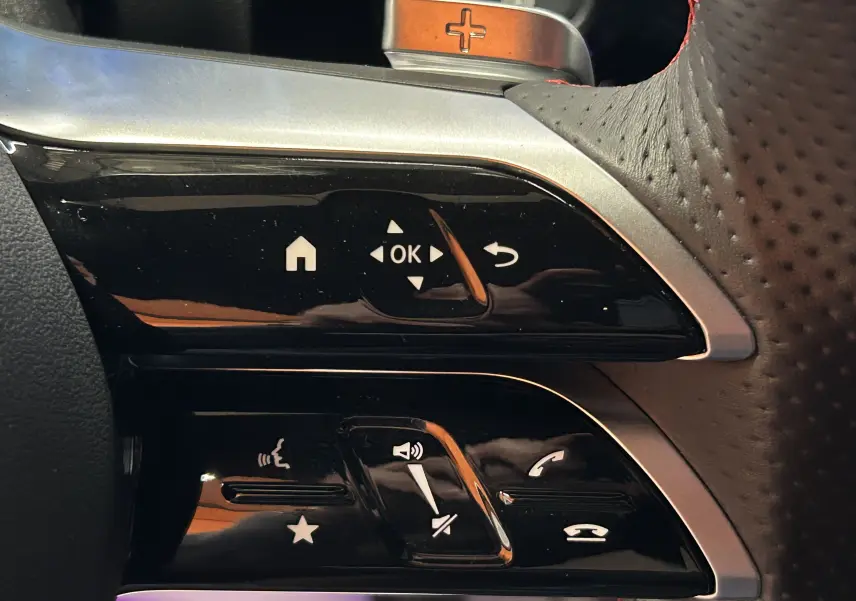 Gros plan sur les commandes noires et argentées du volant perforé côté gauche d'une Mercedes CLA Shooting Brake noire.