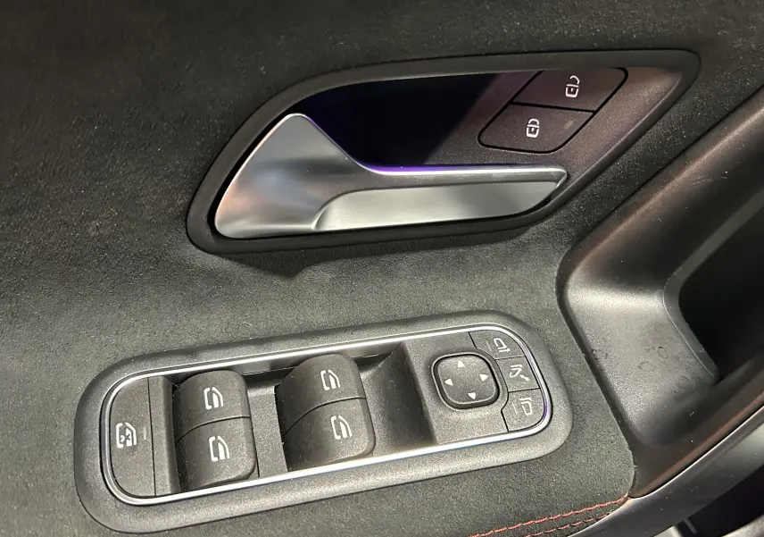 Gros plan sur la poignée intérieure et les commandes des vitres côté conducteur d'une Mercedes CLA Shooting Brake noir métallisé.