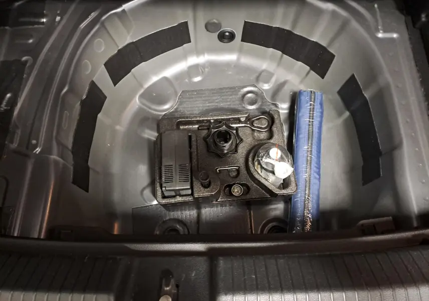 Vue plongeante sur le coffre d'une Volkswagen Polo 2023 gris cendré, montrant le rangement sous le plancher avec outils et kit de réparation.