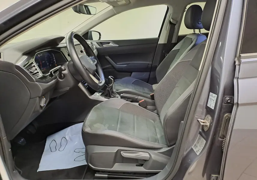 Vue intérieure côté conducteur d'une Volkswagen Polo gris cendré 2023, montrant sièges, volant et tableau de bord numérique.