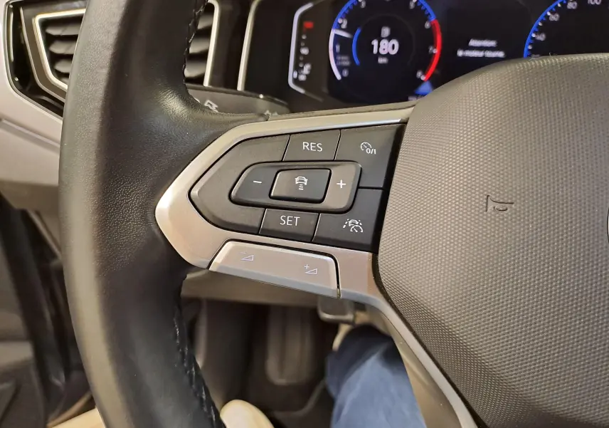 Gros plan sur le volant gauche d'une Volkswagen Polo 2023 avec commandes de régulateur et tableau de bord digital.