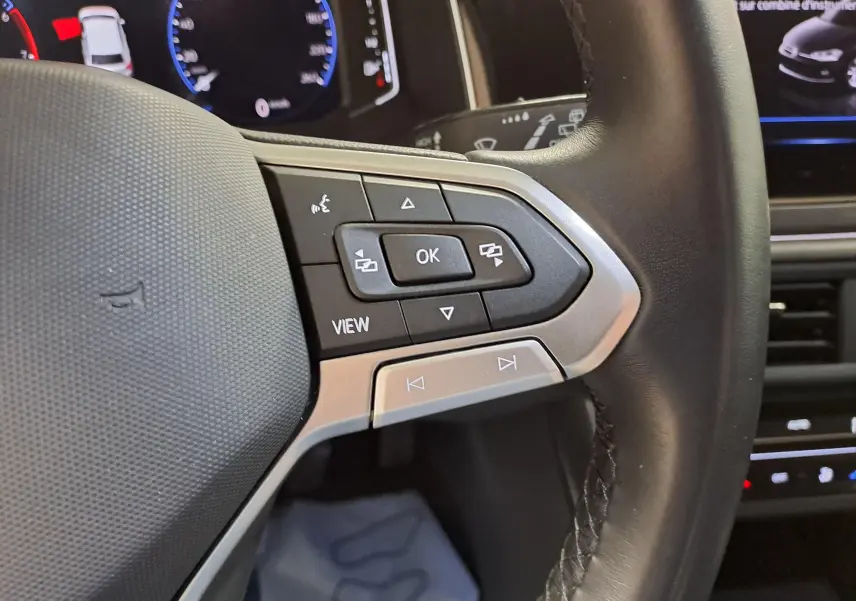 Gros plan sur les commandes au volant cuir noir de la Volkswagen Polo 2023, avec affichage digital en arrière-plan.
