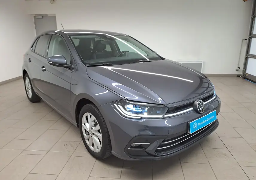 Volkswagen Polo 2023 gris cendré vue 3/4 avant droit avec phares allumés et vitres arrière surteintées.