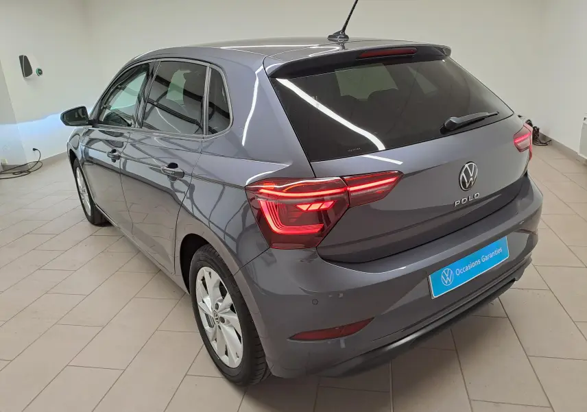 Vue 3/4 arrière d'une Volkswagen Polo gris cendré métallisé avec vitres arrière surteintées dans un showroom.