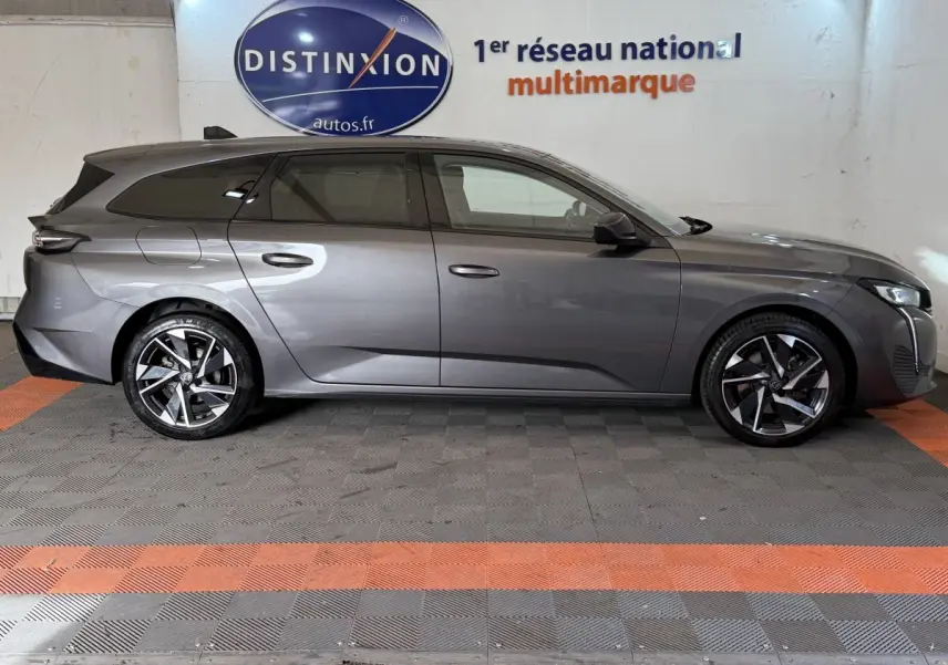 Peugeot 308 SW gris foncé vue de profil côté gauche, avec jantes alliage et toit noir en arrière-plan intérieur showroom.