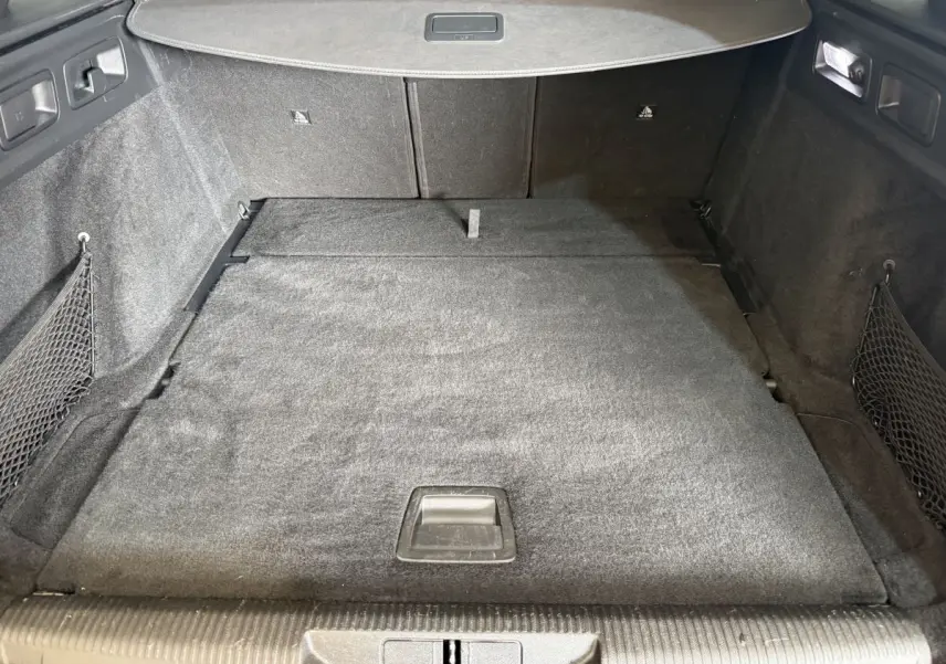 Vue intérieure du coffre spacieux et plat de la Peugeot 308 SW gris foncé, avec filet de rangement latéral et éclairage intégré.