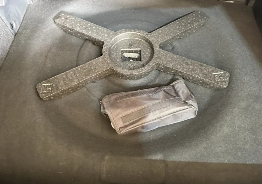 Vue rapprochée du coffre d’une Peugeot 308 gris foncé, montrant un rangement avec une trousse noire posée dessus.