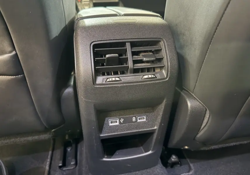Vue rapprochée de la ventilation arrière et des ports USB intégrés entre les sièges noirs d’une Peugeot 308 SW gris foncé.