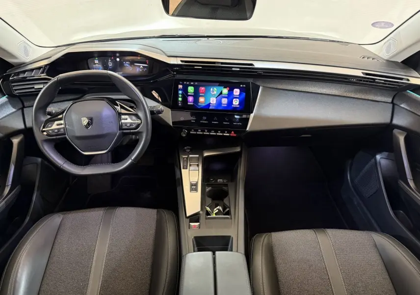 Vue intérieure frontale du tableau de bord et volant cuir noir de la Peugeot 308 SW 2022 avec écran tactile central allumé.