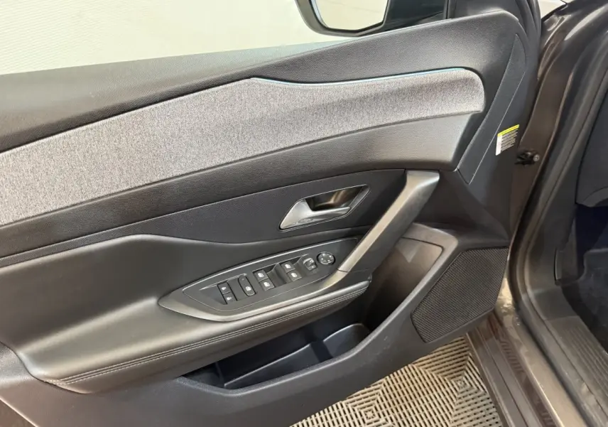 Vue rapprochée de la porte avant gauche de la Peugeot 308 gris foncé, avec commandes électriques et habillage tissu.