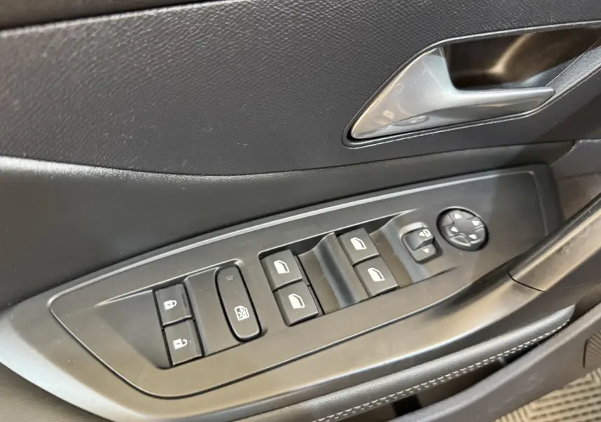 Gros plan sur les commandes des vitres et rétroviseurs côté conducteur de la Peugeot 308 gris foncé, intérieur noir.