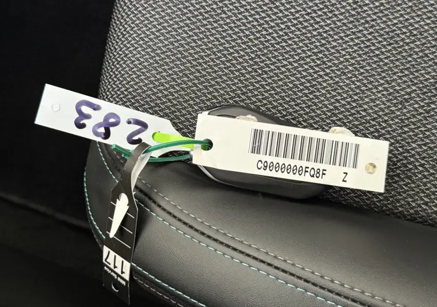 Gros plan sur la clé avec étiquette posée sur un siège tissu gris foncé et cuir noir à surpiqûres bleues du Peugeot 308 SW 2022.