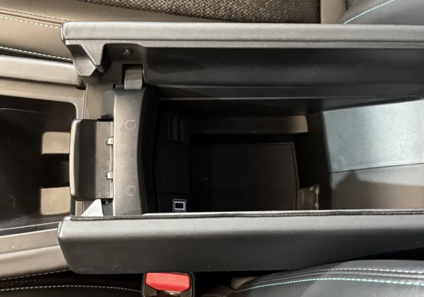 Vue intérieure en plongée sur le rangement central ouvert d'une Peugeot 308 SW gris foncé, avec coutures bleues visibles sur le siège.