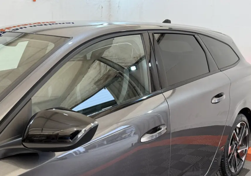 Vue côté gauche avant d'une Peugeot 308 SW gris foncé avec rétroviseur noir brillant et vitres teintées.