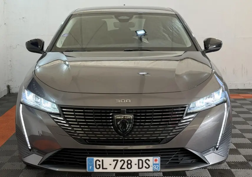 Vue frontale d’une Peugeot 308 gris foncé 2022 avec phares LED allumés et calandre noire distinctive.