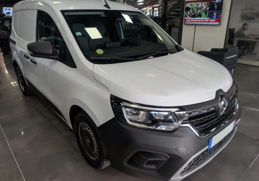 Vue 3/4 avant d'un Renault Kangoo Van blanc minéral avec pare-chocs noir mat et jantes acier en intérieur showroom.