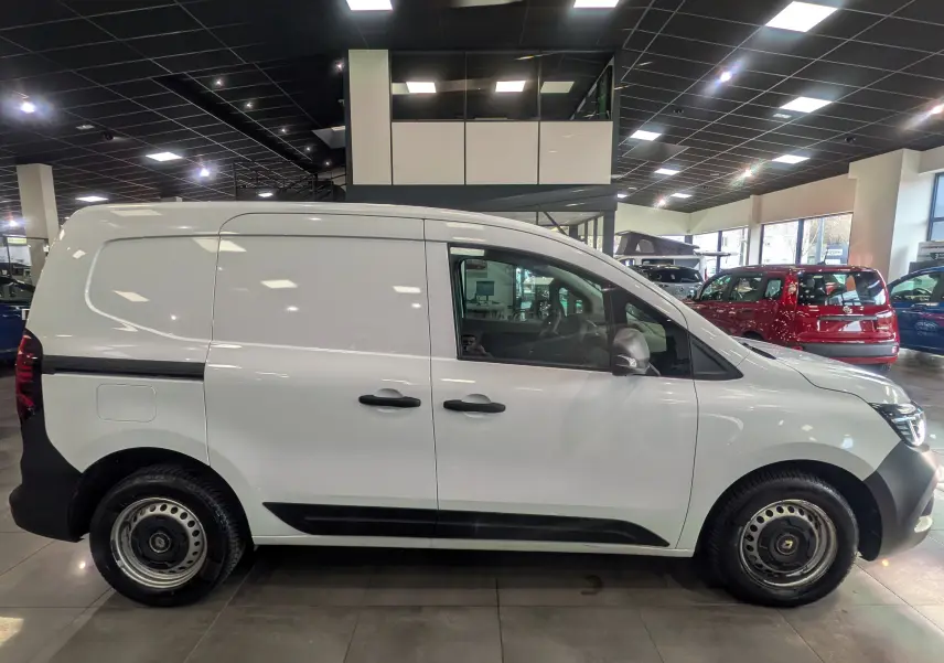Vue de profil côté gauche d’un Renault Kangoo Van blanc minéral avec jantes acier et poignées noires, en intérieur showroom.