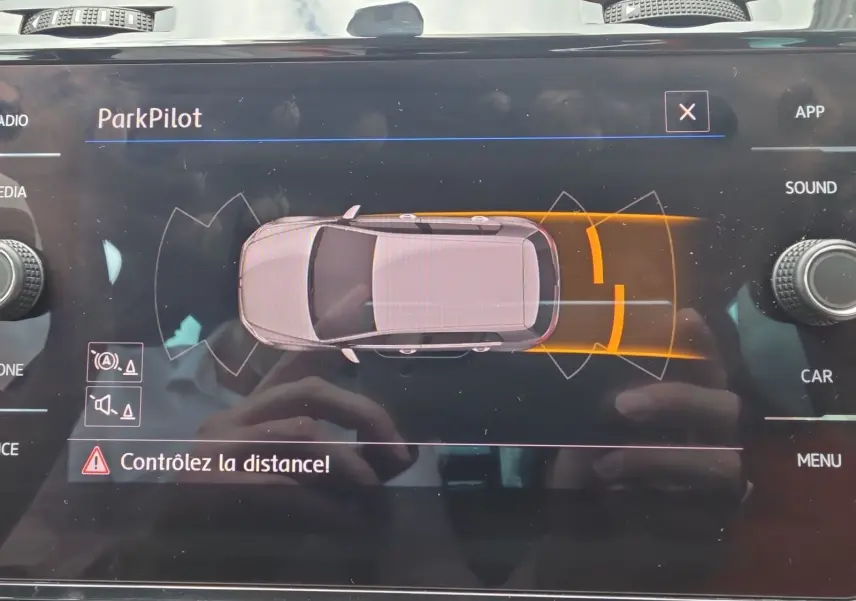 Affichage du système ParkPilot sur l'écran central d'une Volkswagen Golf noire, vue de dessus du véhicule en alerte de proximité arrière.