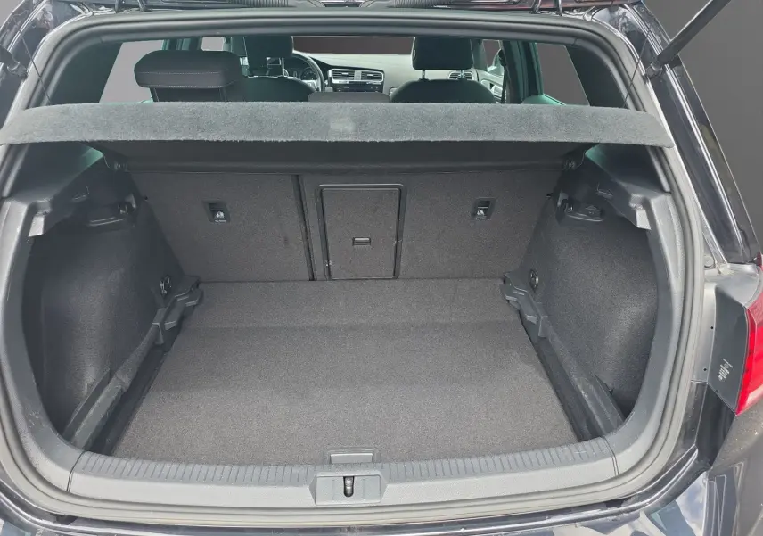 Coffre ouvert vu de l'arrière d'une Volkswagen Golf noire 1.5 TSI EVO 150 R-line, intérieur spacieux et tapis gris.
