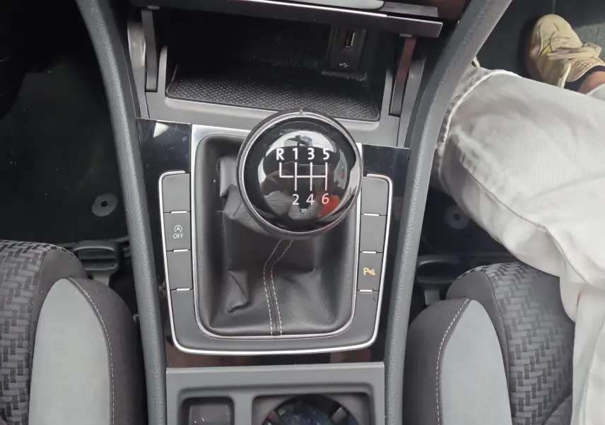 Vue rapprochée du levier de vitesses manuel noir de la Volkswagen Golf 1.5 TSI EVO 150 R-line, avec console centrale et sièges partiellement visibles.