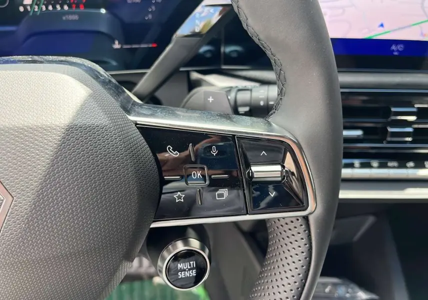 Gros plan sur le volant multifonctions textile de la Renault Clio gris schiste avec commandes intégrées et bouton Multi Sense.