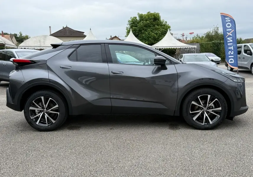 Profil côté gauche du Toyota C-HR 1.8 140CH STYLE 2025 en gris atlas avec jantes alliage et lignes anguleuses marquées.