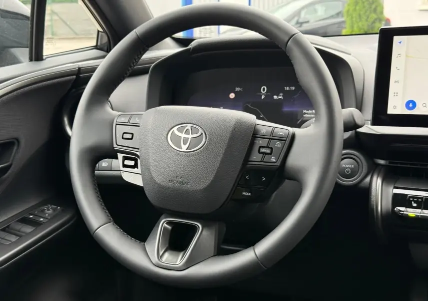 Vue rapprochée du volant multifonction noir du Toyota C-HR 1.8 140CH STYLE MY25 avec tableau de bord digital.