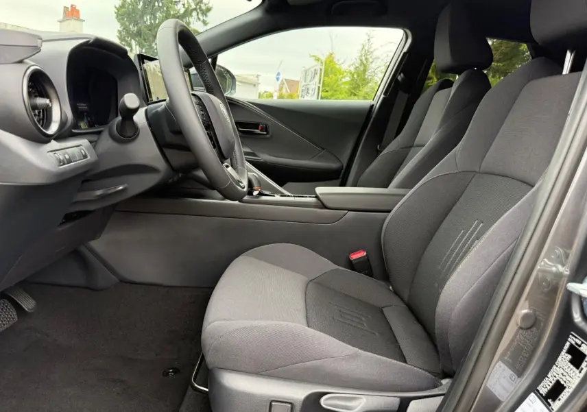 Intérieur avant droit du Toyota C-HR 1.8 140CH STYLE 2025 en gris atlas, sièges tissu gris foncé et tableau de bord moderne.