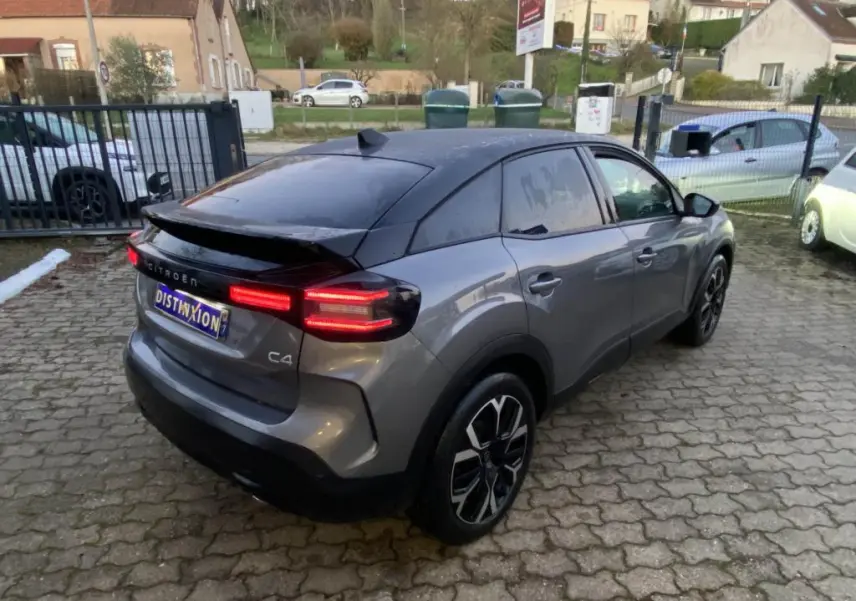 Vue 3/4 arrière droite d'une Citroën C4 2025 gris foncé avec toit noir et feux arrière LED allumés.