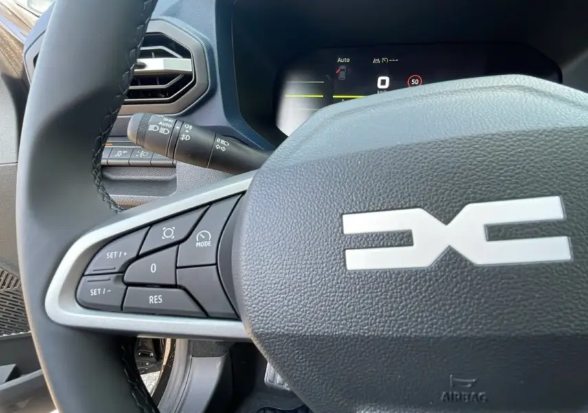 Gros plan sur le volant cuir du Dacia Bigster TCE 130 4x4, avec commandes intégrées et tableau de bord digital visible.