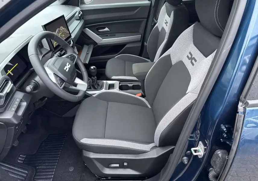 Vue intérieure côté conducteur de la Dacia Bigster bleu indigo, sièges bi-matière avec logo et tableau de bord digital.