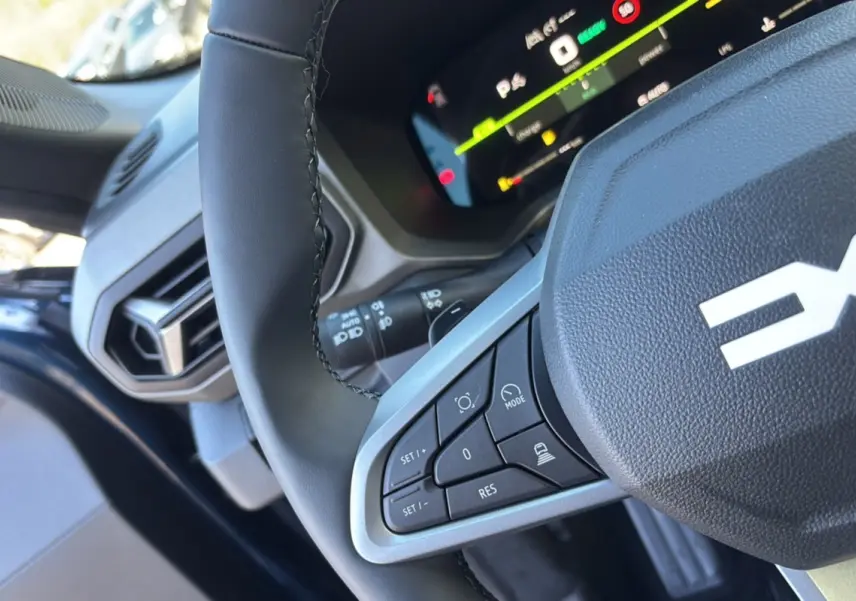 Gros plan sur le volant cuir noir de la Dacia Bigster bleu indigo, avec commandes intégrées et tableau de bord digital visible.