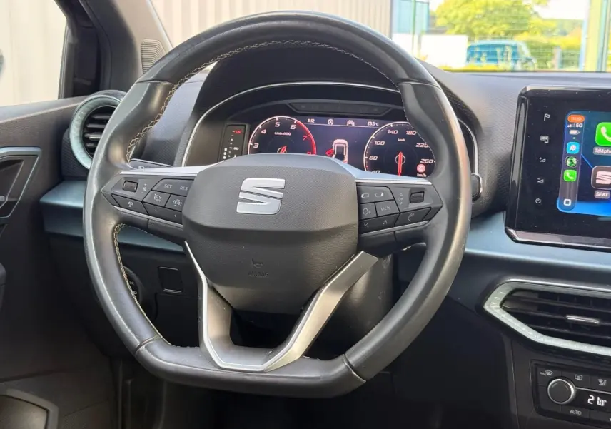 Vue rapprochée du volant en cuir noir avec logo SEAT, tableau de bord numérique et écran tactile central du SEAT Arona 2022.