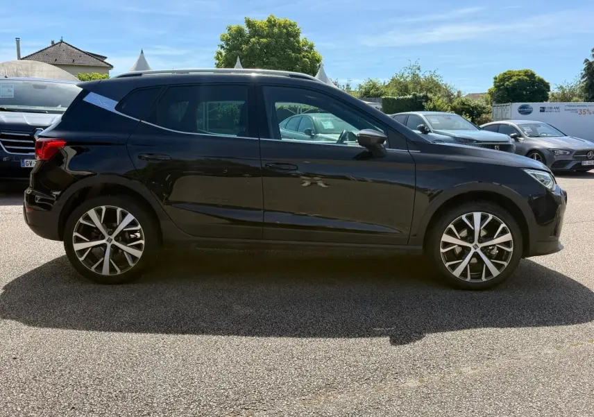 Vue latérale droite d'un SEAT Arona noir 5 portes, avec jantes alliage et toit noir contrasté sous un ciel bleu.