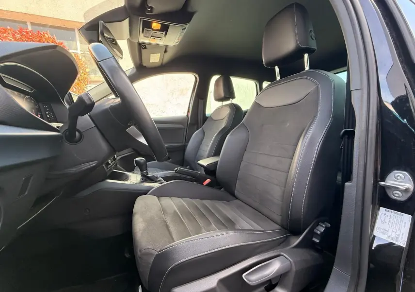 Vue intérieure côté conducteur de la SEAT Arona 2022 avec sièges noirs en tissu et cuir, volant multifonctions visible.