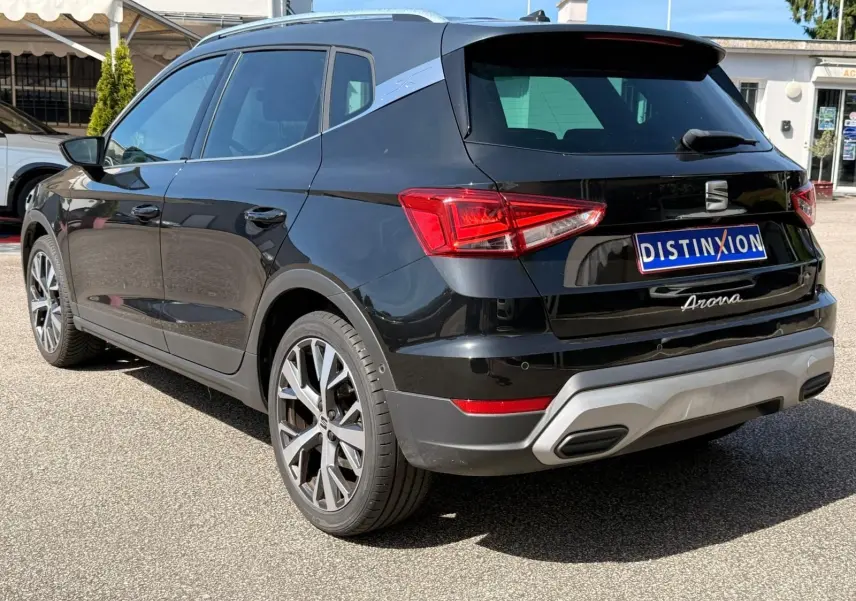 Vue 3/4 arrière droite d'une SEAT Arona noire avec jantes alliage et toit noir mat, stationnée en extérieur.