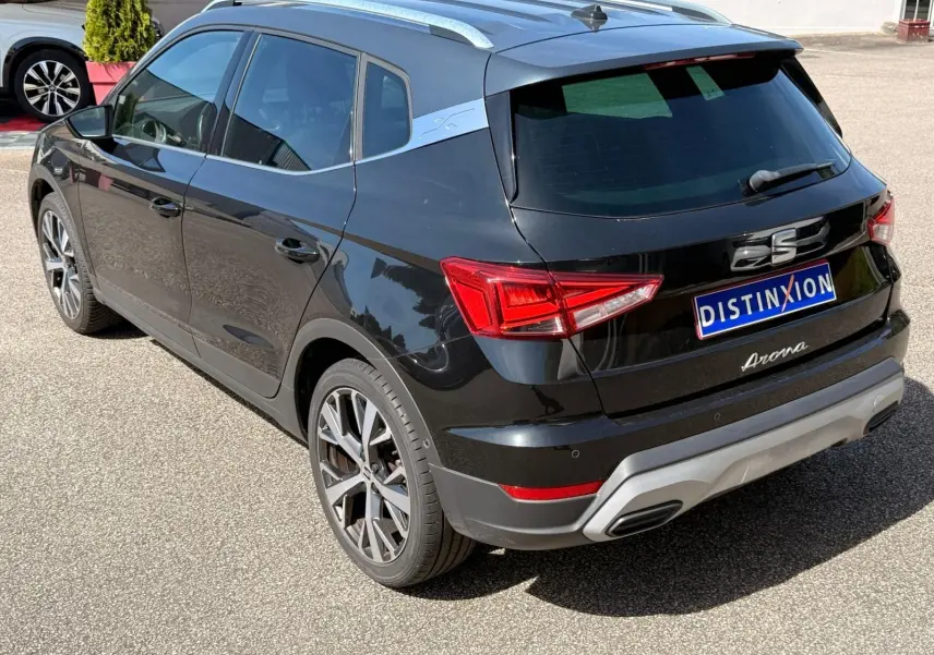 Vue 3/4 arrière droite d'une SEAT Arona noire avec toit et barres de toit argentés, jantes alliage et feux LED distinctifs.
