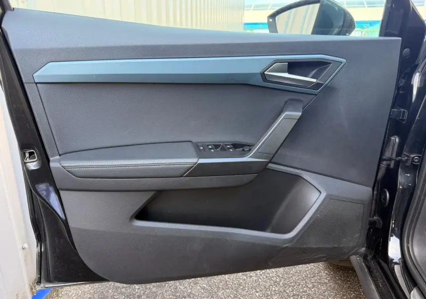 Vue intérieure de la porte avant gauche noire du SEAT Arona 2022 avec commandes de vitres et poignée argentée.