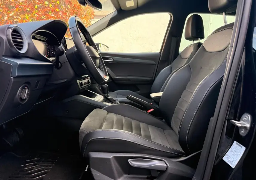 Vue intérieure côté conducteur de la SEAT Arona 2022, sièges noirs avec surpiqûres blanches et volant cuir alu.