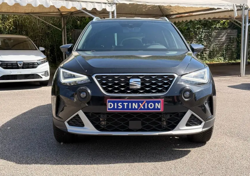 Vue avant d'un SEAT Arona noir avec calandre chromée et plaques Distinxion sous un auvent.