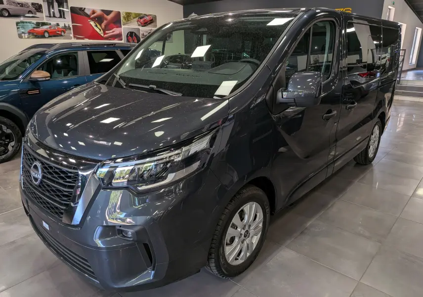 Nissan Primastar Combi gris Comète vue 3/4 avant droit, mettant en valeur sa calandre imposante et ses phares LED modernes.
