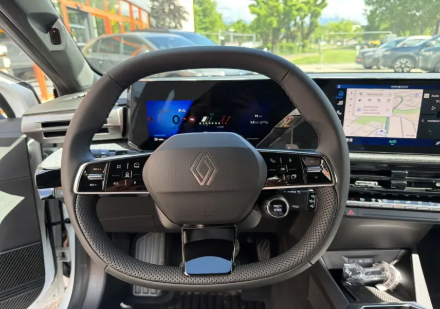 Vue intérieure centrée sur le volant multifonctions de la Renault Clio blanc glacier avec tableau de bord numérique et écran tactile.